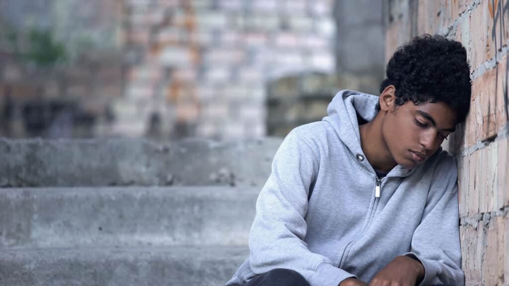 sad, dejected teen leaning his head against brick wall