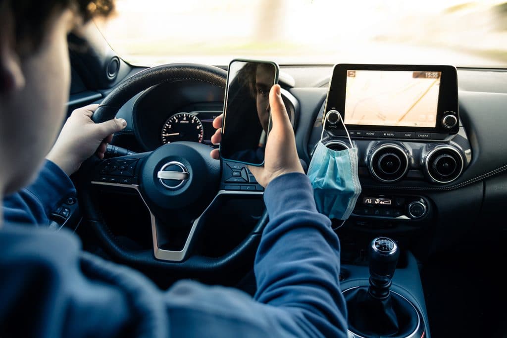 teen boy looking at cell phone behing wheel of car