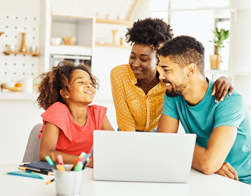 mother and father smiling with daughter in front of laptop