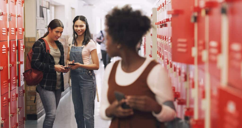 two girls bullying another girl in school hallway with cellphones