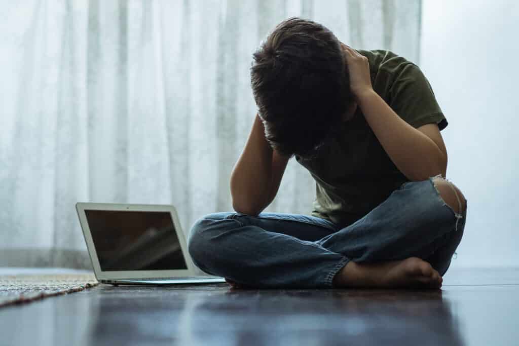 young boy with head in hands with open laptop